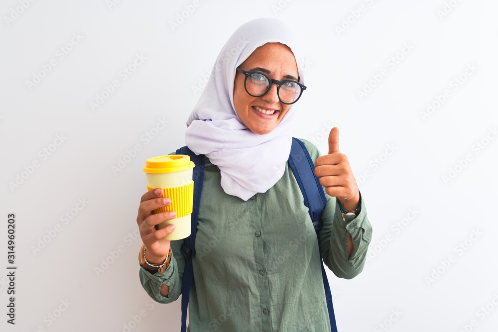 Young Arab student woman wearing hijab and drinking coffee over isolated background happy with big smile doing ok sign, thumb up with fingers, excellent sign Young Arab student woman wearing hijab and drinking coffee over isolated background happy with big smile doing ok sign, thumb up with fingers, excellent sign