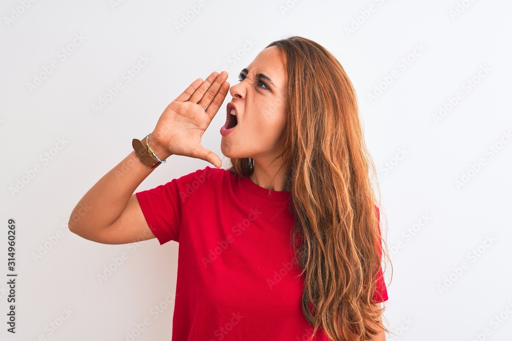 Young redhead woman wearing red casual t-shirt stading over white isolated background shouting and screaming loud to side with hand on mouth. Communication concept. Young redhead woman wearing red casual t-shirt stading over white isolated background shouting and screaming loud to side with hand on mouth. Communication concept.
