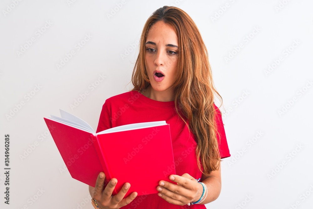 Young beautiful redhead woman reading a red book over isolated background scared in shock with a surprise face, afraid and excited with fear expression Young beautiful redhead woman reading a red book over isolated background scared in shock with a surprise face, afraid and excited with fear expression