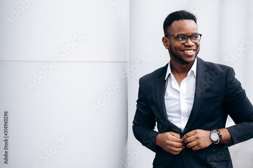 Attractive african american businessman in stylish suit is fastens his jacket and smiling, outdoors