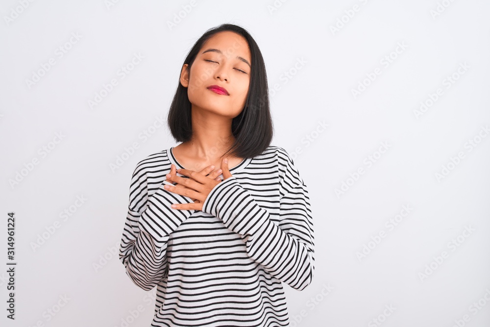 Young chinese woman wearing striped t-shirt standing over isolated white background smiling with hands on chest with closed eyes and grateful gesture on face. Health concept. Young chinese woman wearing striped t-shirt standing over isolated white background smiling with hands on chest with closed eyes and grateful gesture on face. Health concept.