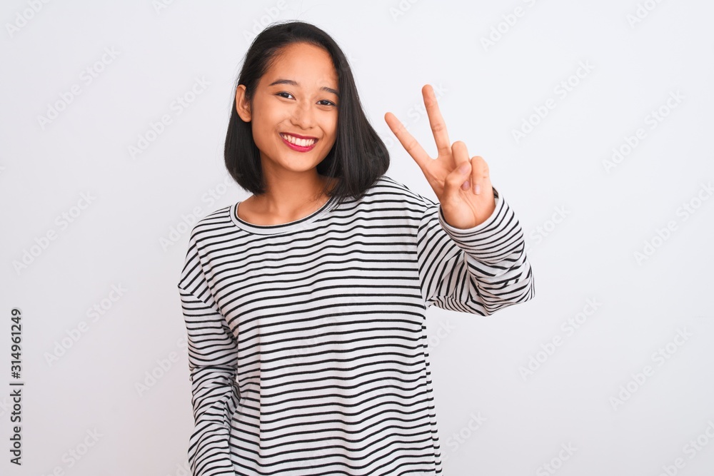 Young chinese woman wearing striped t-shirt standing over isolated white background smiling looking to the camera showing fingers doing victory sign. Number two. Young chinese woman wearing striped t-shirt standing over isolated white background smiling looking to the camera showing fingers doing victory sign. Number two.