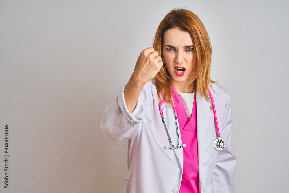 Redhead caucasian doctor woman wearing pink stethoscope over isolated background angry and mad raising fist frustrated and furious while shouting with anger. Rage and aggressive concept. Redhead caucasian doctor woman wearing pink stethoscope over isolated background angry and mad raising fist frustrated and furious while shouting with anger. Rage and aggressive concept.