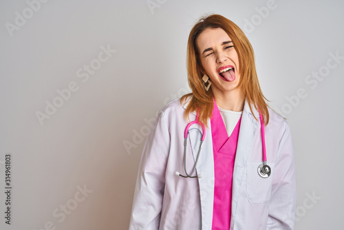 Redhead caucasian doctor woman wearing pink stethoscope over isolated background sticking tongue out happy with funny expression. Emotion concept.