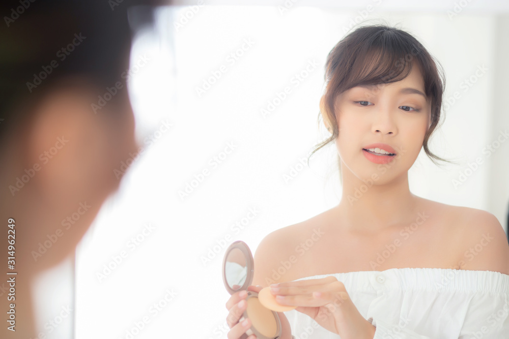 Portrait beautiful young asian woman applying powder puff at cheek makeup of cosmetic looking mirror, beauty of girl with skin face smile in the bedroom, health and wellness concept. Portrait beautiful young asian woman applying powder puff at cheek makeup of cosmetic looking mirror, beauty of girl with skin face smile in the bedroom, health and wellness concept.