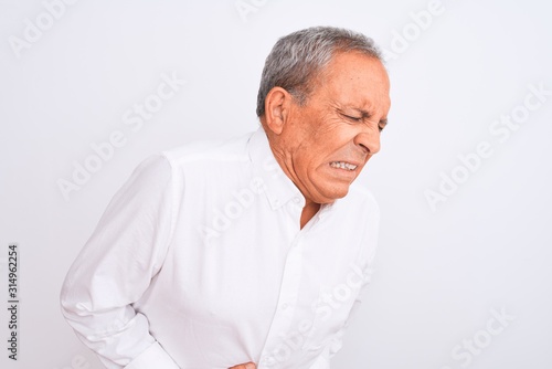 Senior grey-haired man wearing elegant shirt standing over isolated white background with hand on stomach because indigestion, painful illness feeling unwell. Ache concept.