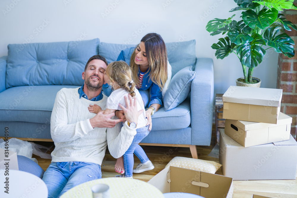 Beautiful family, parents sitting on the sofa drinking coffee looking his kid playing at new home around cardboard boxes Beautiful family, parents sitting on the sofa drinking coffee looking his kid playing at new home around cardboard boxes
