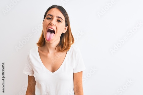 Photo Beautiful redhead woman wearing casual white t-shirt over isolated background sticking tongue out happy with funny expression