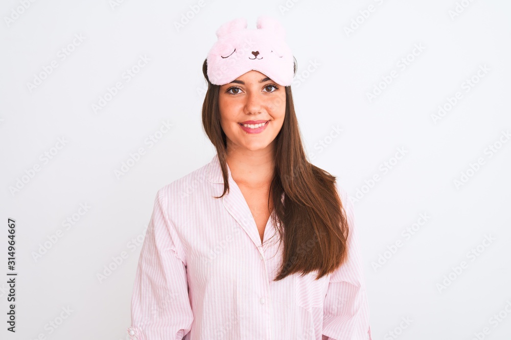 Young beautiful girl wearing pajama and sleep mask standing over isolated white background with a happy and cool smile on face. Lucky person. Young beautiful girl wearing pajama and sleep mask standing over isolated white background with a happy and cool smile on face. Lucky person.