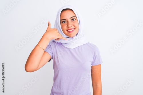 Young beautiful arabian girl wearing hijab standing over isolated white background smiling doing phone gesture with hand and fingers like talking on the telephone. Communicating concepts. © Krakenimages.com