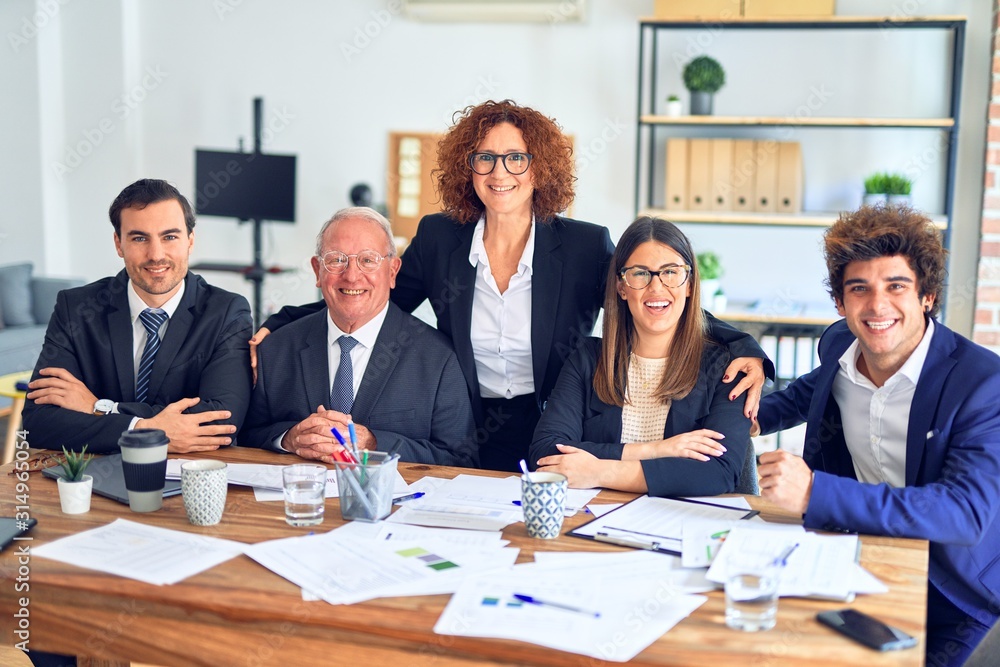 Group of business workers smiling happy and confident in a meeting. The boss standing and employees sitting with smile on face looking at the camera at the office Group of business workers smiling happy and confident in a meeting. The boss standing and employees sitting with smile on face looking at the camera at the office