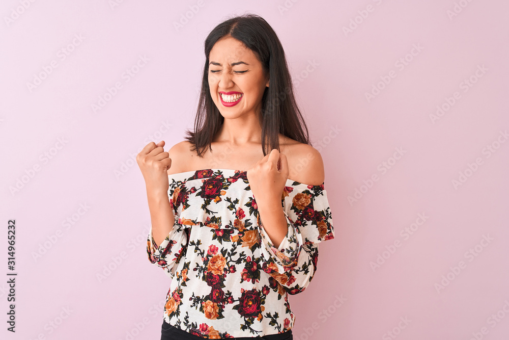 Young chinese woman wearing floral t-shirt standing over isolated pink background very happy and excited doing winner gesture with arms raised, smiling and screaming for success. Celebration concept. Young chinese woman wearing floral t-shirt standing over isolated pink background very happy and excited doing winner gesture with arms raised, smiling and screaming for success. Celebration concept.