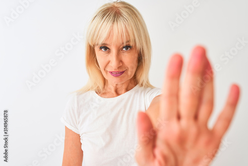 Middle age woman wearing casual t-shirt standing over isolated white background with open hand doing stop sign with serious and confident expression, defense gesture