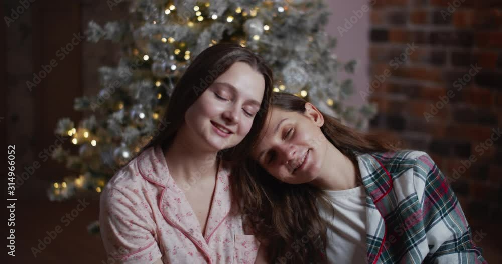 Two happy women are sitting on the background of the New Year tree and smiling. Female portrait, close-up. Merry christmas concept Two happy women are sitting on the background of the New Year tree and smiling. Female portrait, close-up. Merry christmas concept