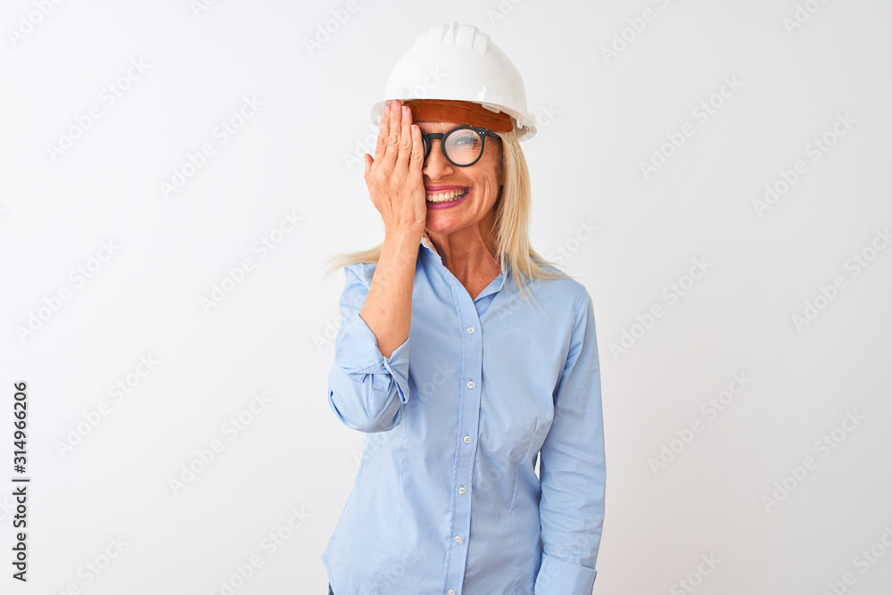 Middle age architect woman wearing glasses and helmet over isolated white background covering one eye with hand, confident smile on face and surprise emotion. Middle age architect woman wearing glasses and helmet over isolated white background covering one eye with hand, confident smile on face and surprise emotion.