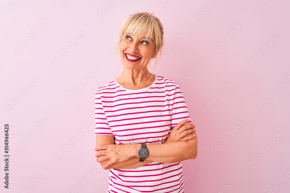 Middle age woman wearing striped t-shirt standing over isolated pink background smiling looking to the side and staring away thinking. Middle age woman wearing striped t-shirt standing over isolated pink background smiling looking to the side and staring away thinking.
