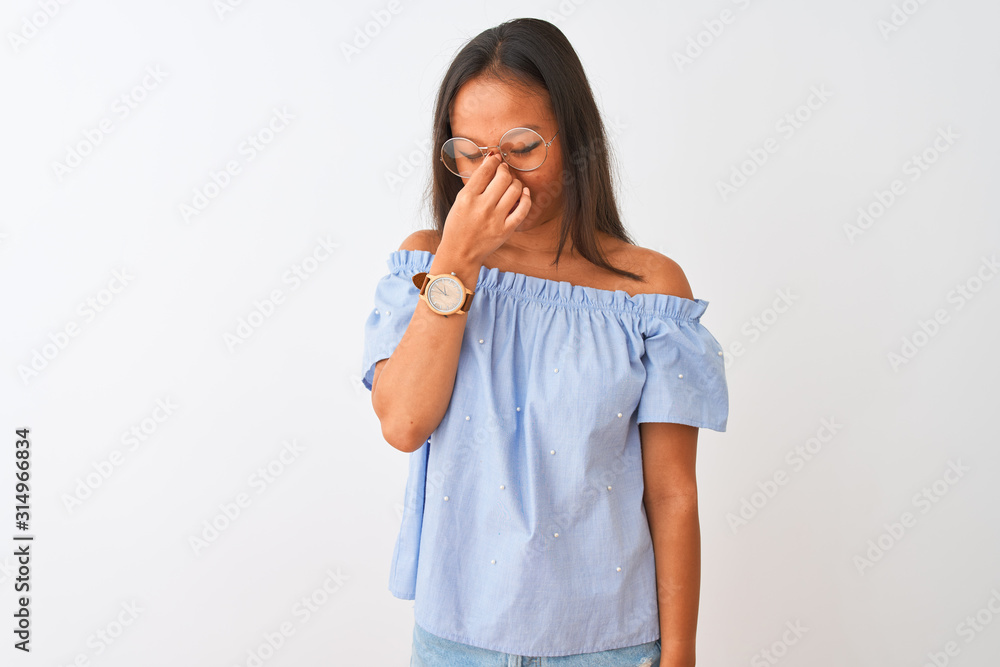 Young chinese woman wearing blue t-shirt and glasses over isolated white background tired rubbing nose and eyes feeling fatigue and headache. Stress and frustration concept. Young chinese woman wearing blue t-shirt and glasses over isolated white background tired rubbing nose and eyes feeling fatigue and headache. Stress and frustration concept.