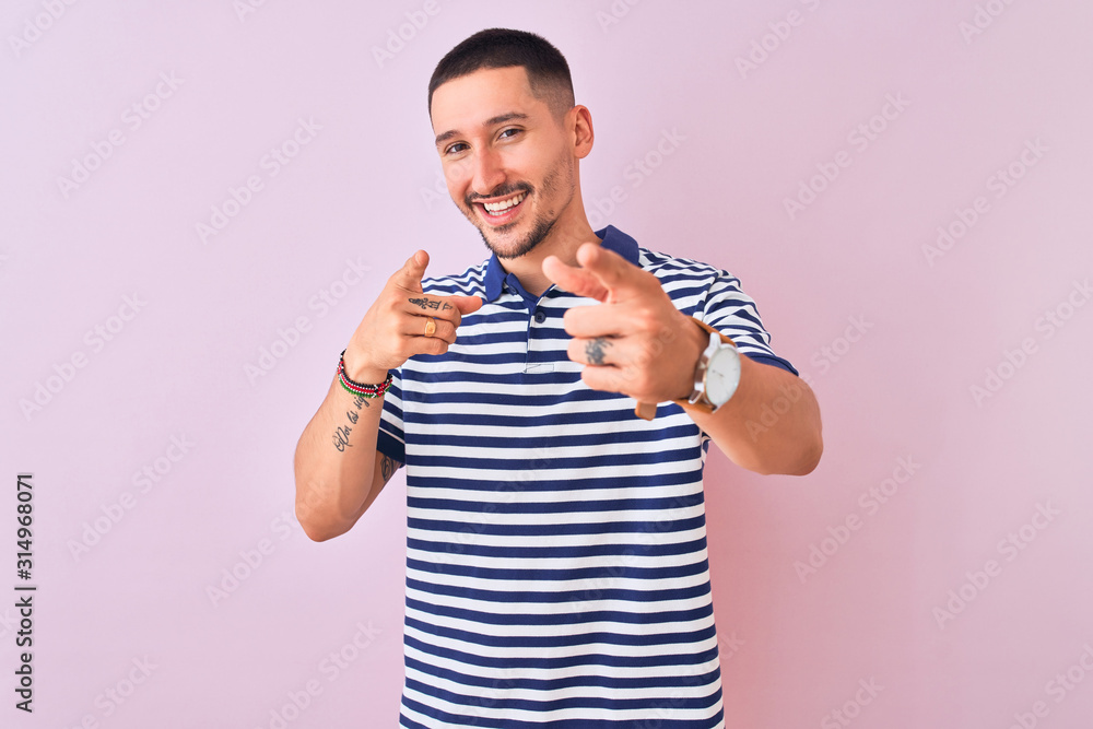 Young handsome man wearing nautical striped t-shirt over pink isolated background pointing fingers to camera with happy and funny face. Good energy and vibes. Young handsome man wearing nautical striped t-shirt over pink isolated background pointing fingers to camera with happy and funny face. Good energy and vibes.