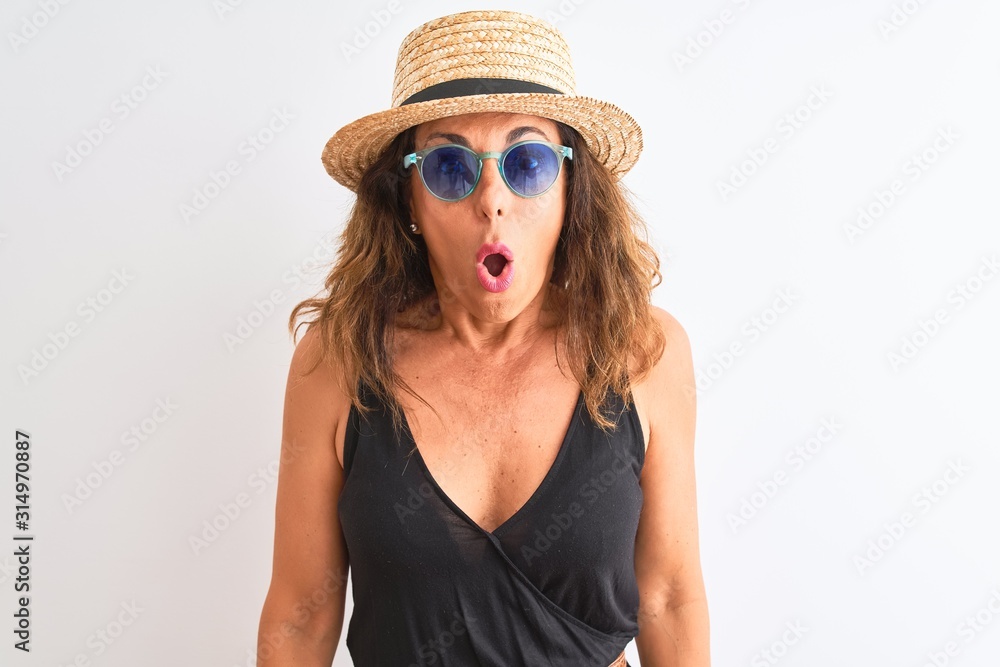 Middle age woman wearing black t-shirt sunglasses and hat over isolated white background scared in shock with a surprise face, afraid and excited with fear expression Middle age woman wearing black t-shirt sunglasses and hat over isolated white background scared in shock with a surprise face, afraid and excited with fear expression