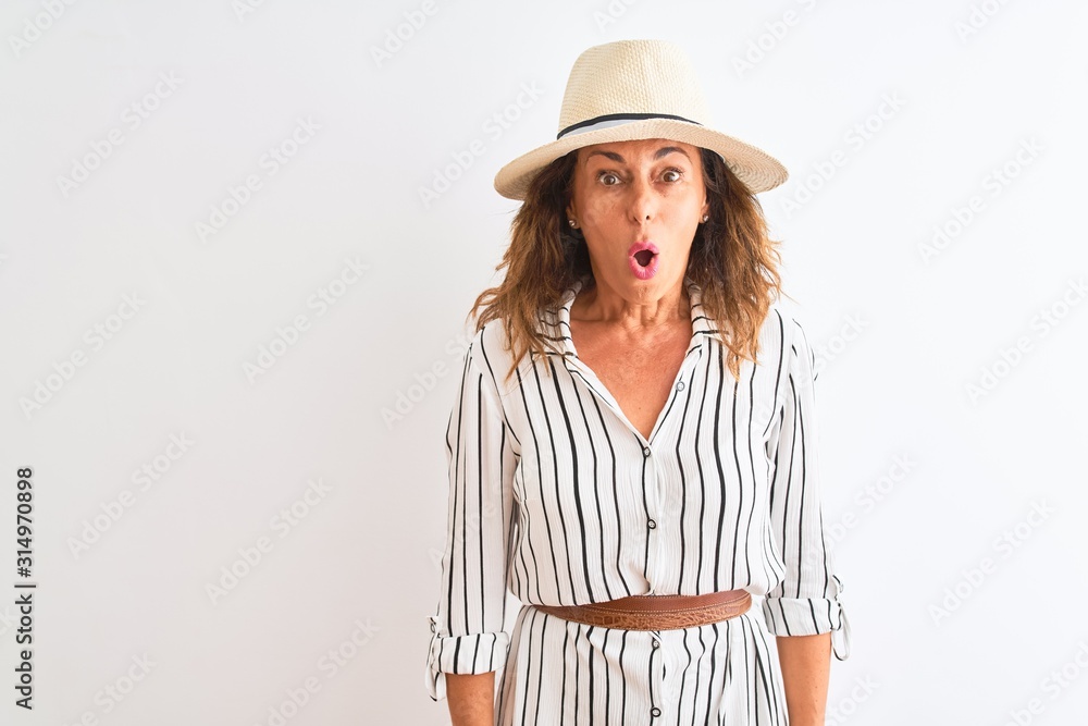 Middle age businesswoman wearing striped dress and hat over isolated white background afraid and shocked with surprise expression, fear and excited face. Middle age businesswoman wearing striped dress and hat over isolated white background afraid and shocked with surprise expression, fear and excited face.
