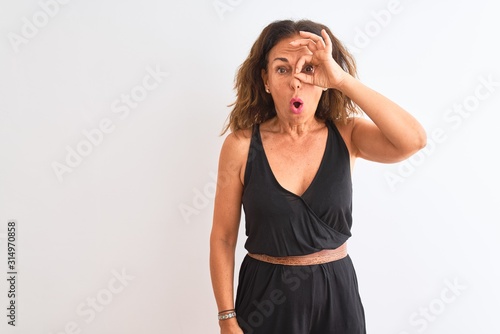 Middle age woman wearing black casual dress standing over isolated white background doing ok gesture shocked with surprised face, eye looking through fingers. Unbelieving expression. © Krakenimages.com