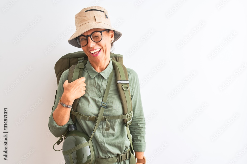 Fototapeta premium Middle age hiker woman wearing backpack canteen hat glasses over isolated white background winking looking at the camera with sexy expression, cheerful and happy face.