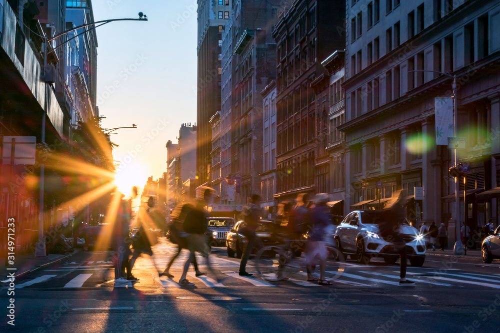 Rays of sunset shine on the diverse crowds of people walking through a busy intersection in New York City