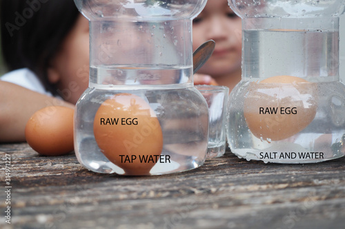 kids easy experiment at home.Asian siblings kid making Salty Science with Floating Eggs in Water.Kid put an egg in tap water versus water that added enough salt.Then they observed for the result, photo