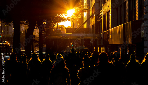 The silhouettes of people are illuminated by the bright light of sunset on the sidewalks of New York City