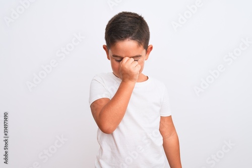 Beautiful kid boy wearing casual t-shirt standing over isolated white background tired rubbing nose and eyes feeling fatigue and headache. Stress and frustration concept.