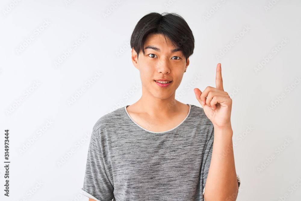 Young chinese man wearing casual t-shirt standing over isolated white background surprised with an idea or question pointing finger with happy face, number one