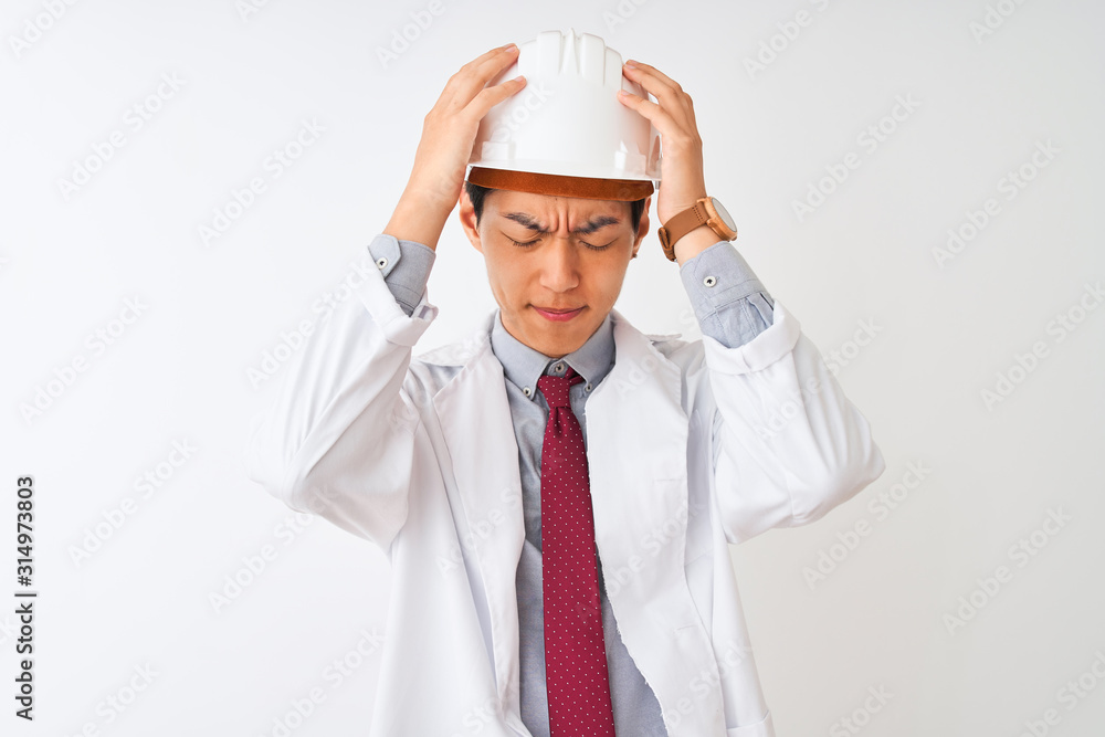 Chinese architect man wearing coat and helmet standing over isolated white background suffering from headache desperate and stressed because pain and migraine. Hands on head. Chinese architect man wearing coat and helmet standing over isolated white background suffering from headache desperate and stressed because pain and migraine. Hands on head.