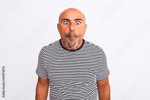 Middle age handsome man wearing striped navy t-shirt over isolated white background making fish face with lips, crazy and comical gesture. Funny expression.