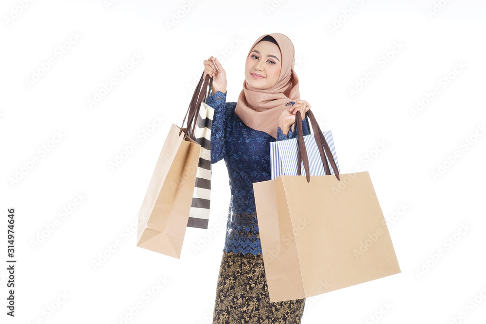 A beautiful and excited Muslim female model in a Asian traditional dress modern kurung carrying shopping bags isolated on white background. Eidul fitri fashion and festive preparation shopping concept A beautiful and excited Muslim female model in a Asian traditional dress modern kurung carrying shopping bags isolated on white background. Eidul fitri fashion and festive preparation shopping concept