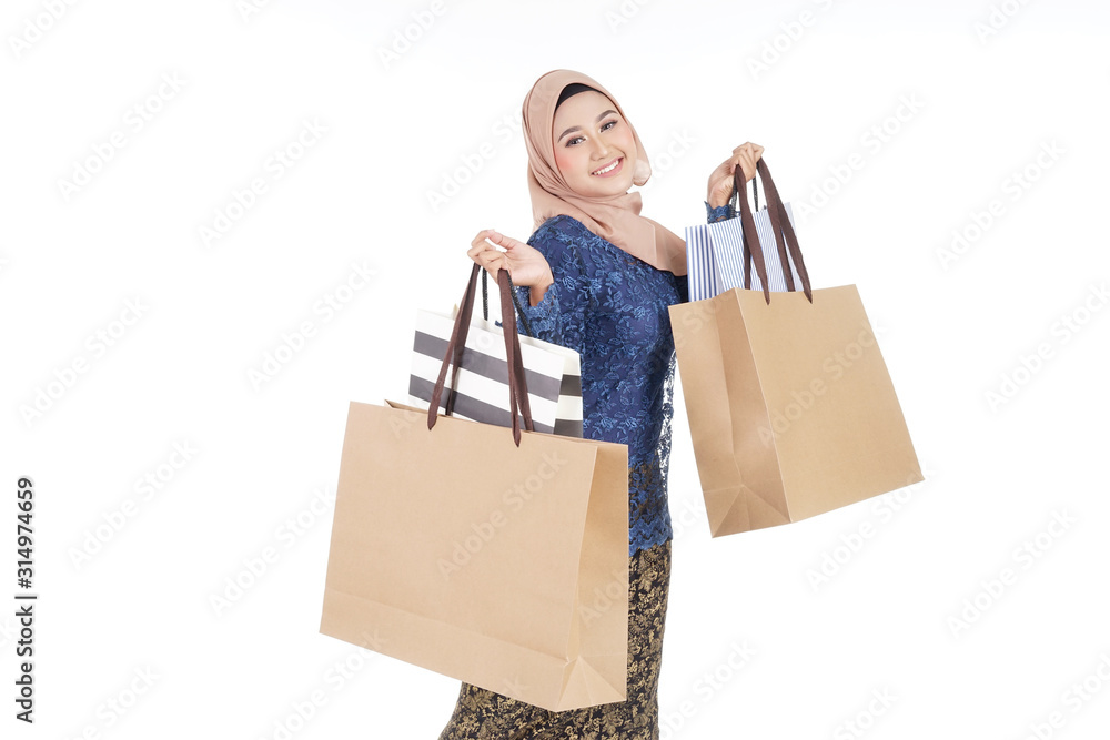 A beautiful and excited Muslim female model in a Asian traditional dress modern kurung carrying shopping bags isolated on white background. Eidul fitri fashion and festive preparation shopping concept A beautiful and excited Muslim female model in a Asian traditional dress modern kurung carrying shopping bags isolated on white background. Eidul fitri fashion and festive preparation shopping concept