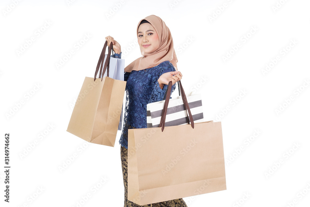 A beautiful and excited Muslim female model in a Asian traditional dress modern kurung carrying shopping bags isolated on white background. Eidul fitri fashion and festive preparation shopping concept A beautiful and excited Muslim female model in a Asian traditional dress modern kurung carrying shopping bags isolated on white background. Eidul fitri fashion and festive preparation shopping concept