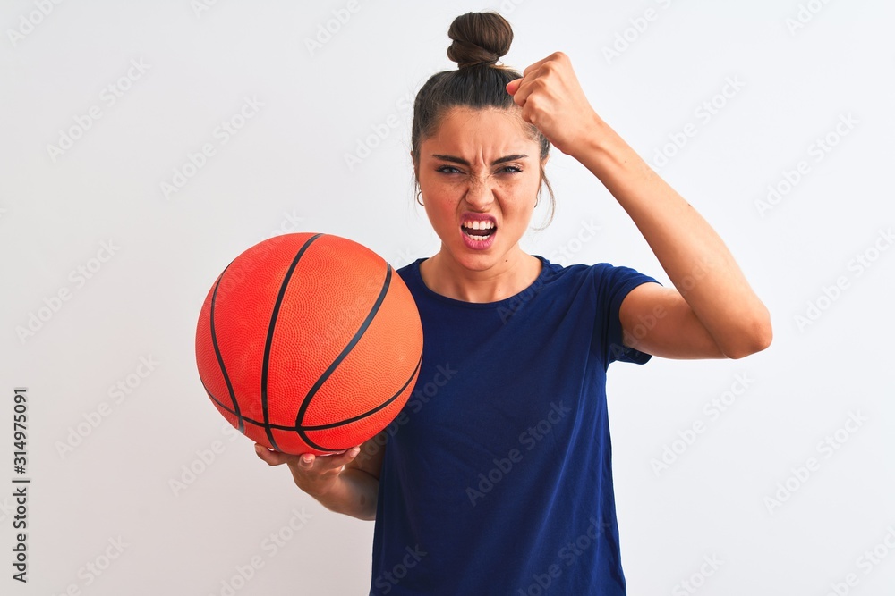 Young beautiful sportswoman holding basketball ball over isolated white background annoyed and frustrated shouting with anger, crazy and yelling with raised hand, anger concept
