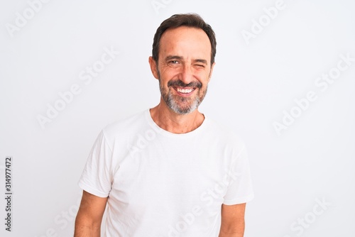 Middle age handsome man wearing casual t-shirt standing over isolated white background winking looking at the camera with sexy expression, cheerful and happy face.