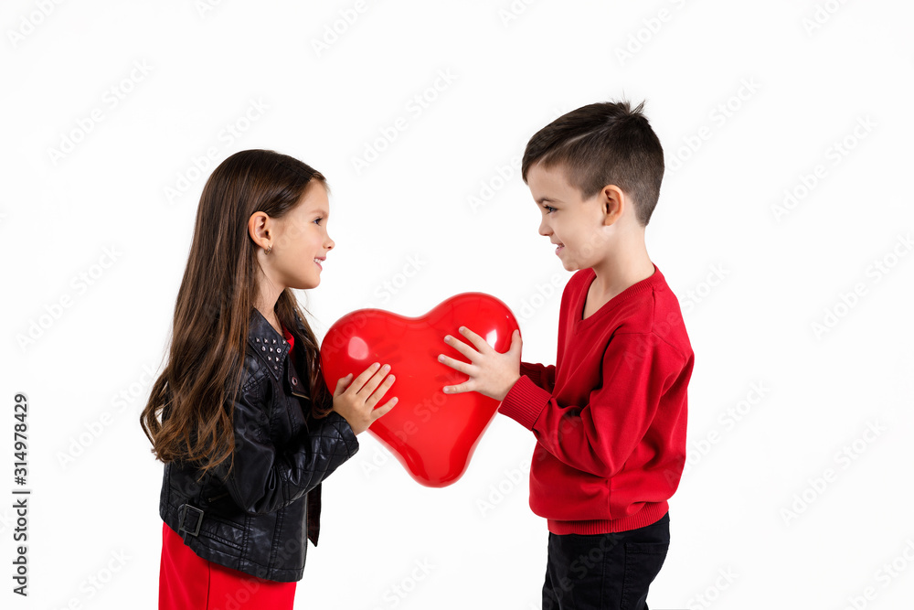 Happy little couple girl and boy holding red heart balloon together isolated on white background. children look at each other. St. Valentine's Day Happy little couple girl and boy holding red heart balloon together isolated on white background. children look at each other. St. Valentine's Day