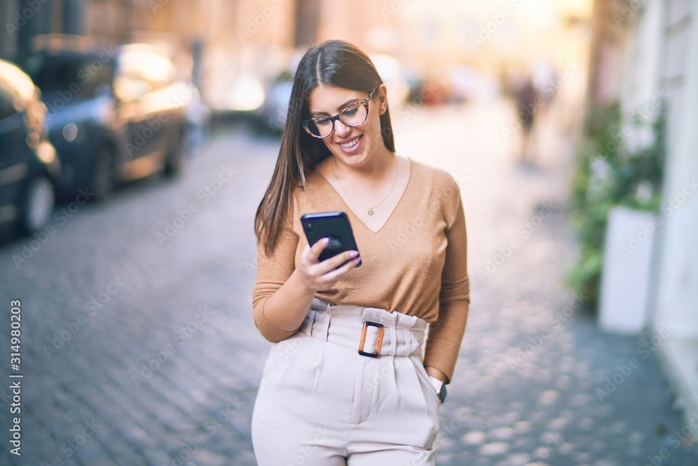 Obraz premium Young beautiful woman smiling happy and confident. Standing with smile on face using smartphone at the city