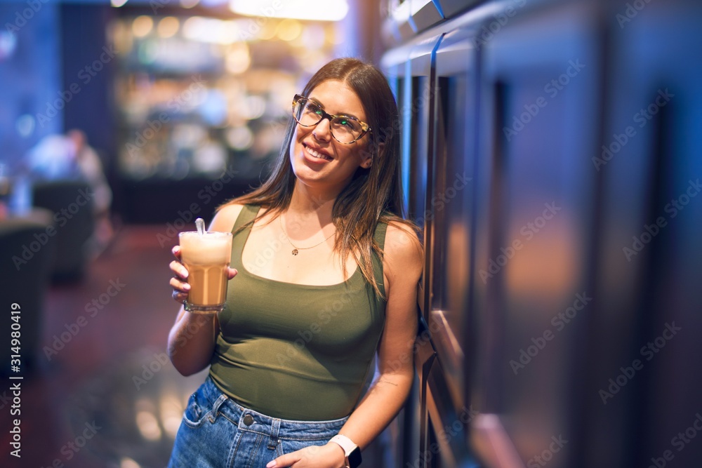 Young beautiful woman smiling happy and confident. Standing with smile on face holding glass of coffee at restaurant