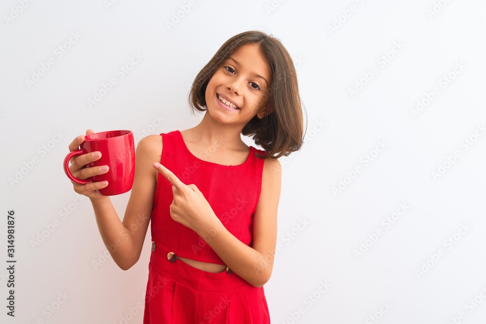 Beautiful child girl holding red cup of tea standing over isolated white background very happy pointing with hand and finger Beautiful child girl holding red cup of tea standing over isolated white background very happy pointing with hand and finger