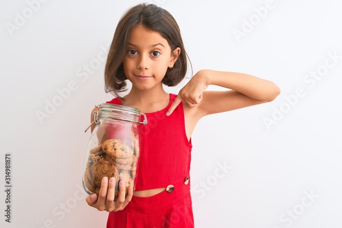 Fotografía Beautiful child girl holding jar of cookies standing over isolated white backgro