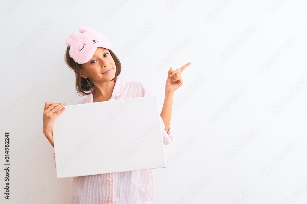 Child girl wearing sleep mask and pajama holding banner over isolated white background very happy pointing with hand and finger to the side Child girl wearing sleep mask and pajama holding banner over isolated white background very happy pointing with hand and finger to the side