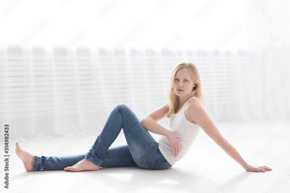 beautiful blonde woman in jeans and a white t-shirt on the floor in a bright room beautiful blonde woman in jeans and a white t-shirt on the floor in a bright room