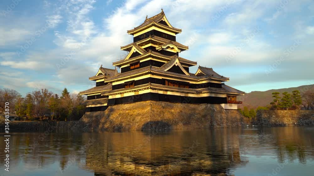The beautiful Matsumoto Castle in Japan during the sunset surrounded with trees a water filled moat - Wide shot