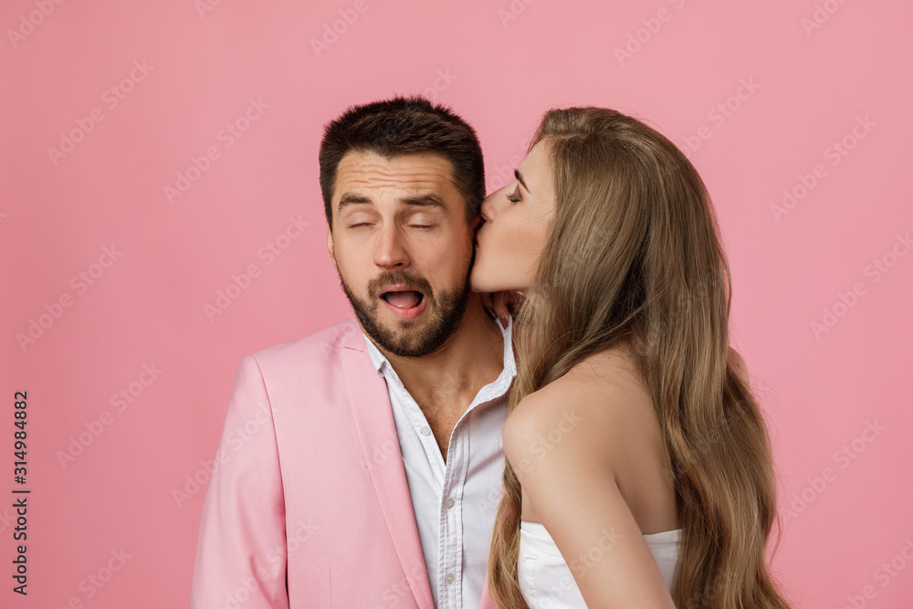 woman kissing her boyfriend. close-up. st valentines day. funny happy couple in love on pink background. woman kissing her boyfriend. close-up. st valentines day. funny happy couple in love on pink background.