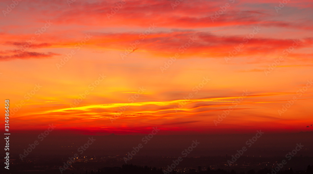 Bergamo, Italy. Fiery sunset over the Po valley and the Alps. Clouds that create light red and orange waves. Fabulous contest. Warm colors