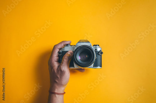 Man's hand holds an old film camera on a yellow bright background