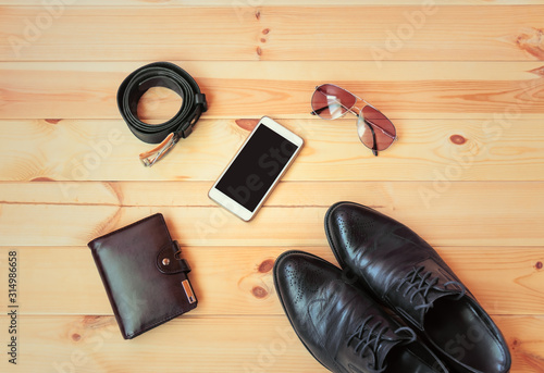 Fashionable black men's shoes, smartphone, wallet, sunglasses and rolled belt on wooden background